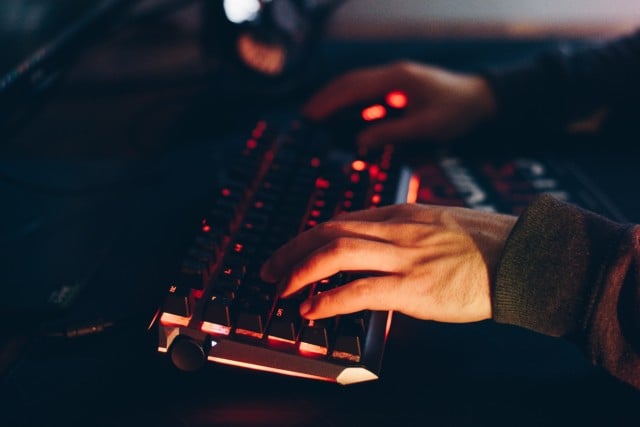 Hacker typing on a backlit keyboard in the dark